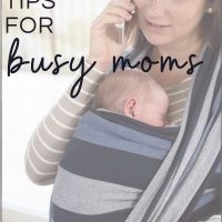 mom on phone using laptop wearing baby in sling