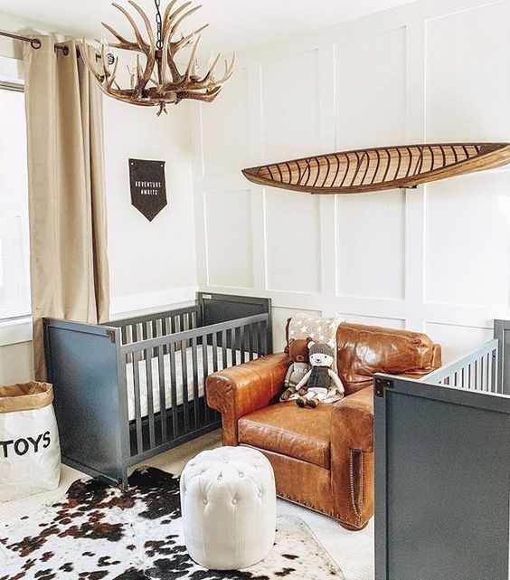 TWINS FARMHOUSE NURSERY WITH GREY CRIBS, A LEATHER CHAIR, AN ANTLER CHANDELIER AND AN ANIMAL SKIN RUG