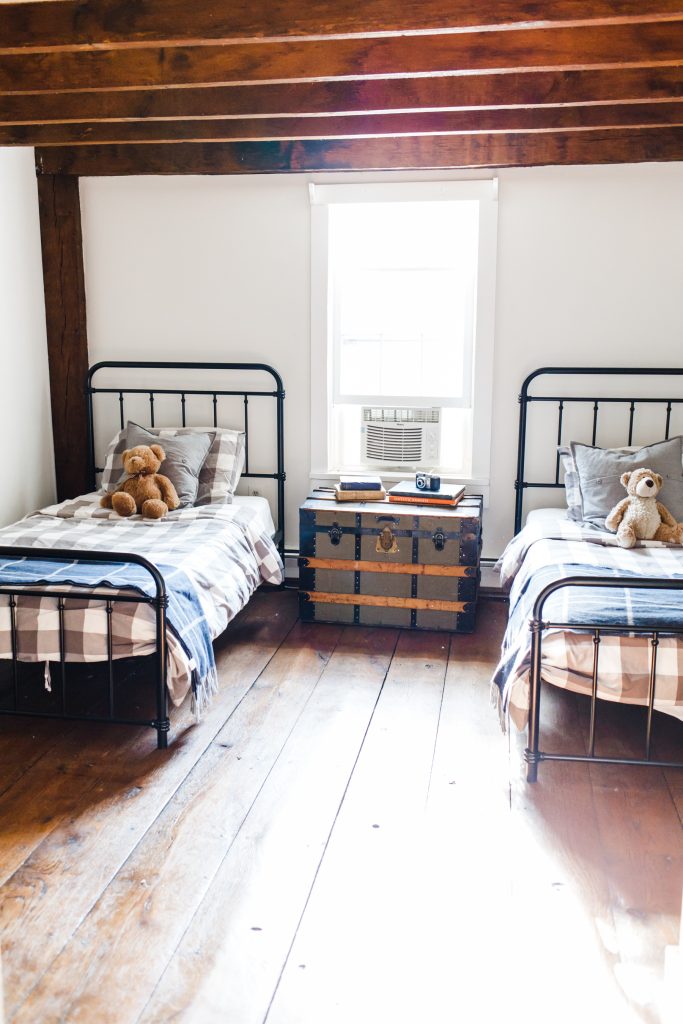 kids shared bedroom with black metal frame beds, wide plank hardwood floors, and exposed ceiling rafters