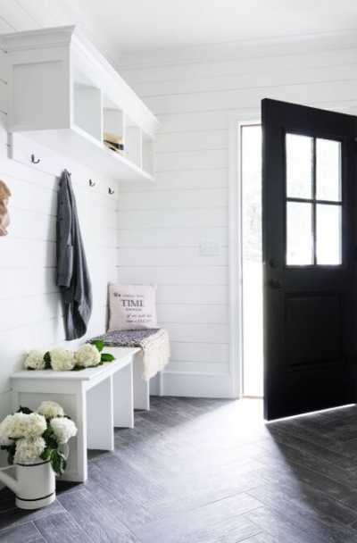 Elegant farmhouse mudroom entrance with natural light, gray herringbone tiles,  white chairs and walls, and a black front door