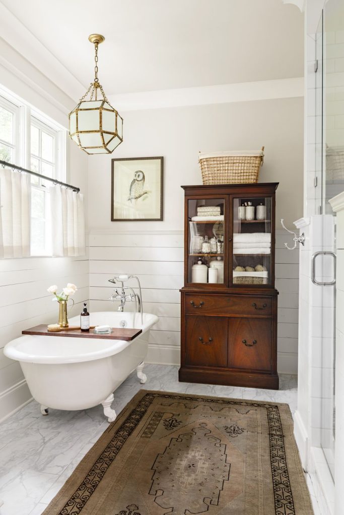 Elegant farmhouse bathroom with vintage wooden hutch as a linen closet and vintage rug